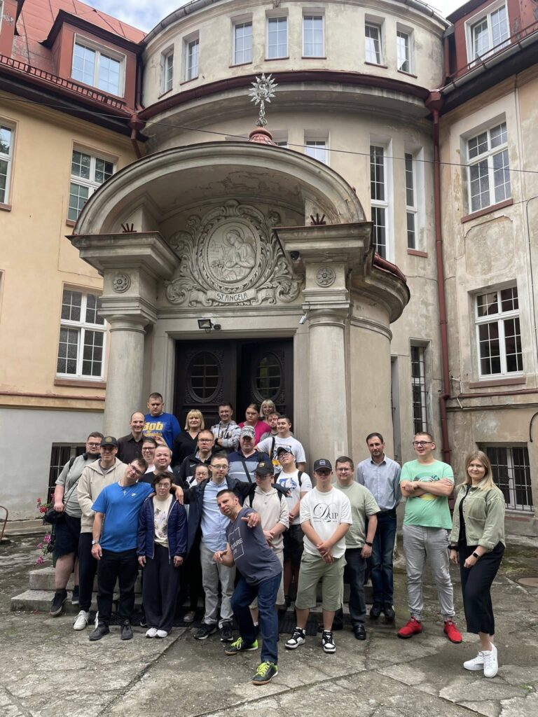 Grupa podopiecznych i opiekunów stojąca na dziedzińcu przed wejściem do zabytkowego, renesansowego budynku z rzeźbionym portalem.