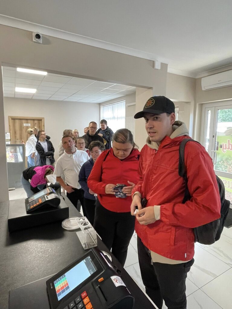 Grupa osób stojąca w kolejce przy kasie w jasnym pomieszczeniu sklepu 