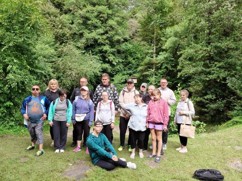 Duża grupa osób pozująca do zdjęcia w lesie lub na skraju gęstego, zielonego zagajnika.