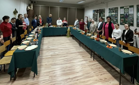 Widok na salę przygotowaną do spotkania. Uczestnicy stoją wokół stołów ustawionych w kształt litery U, na których przygotowano poczęstunek i napoje.