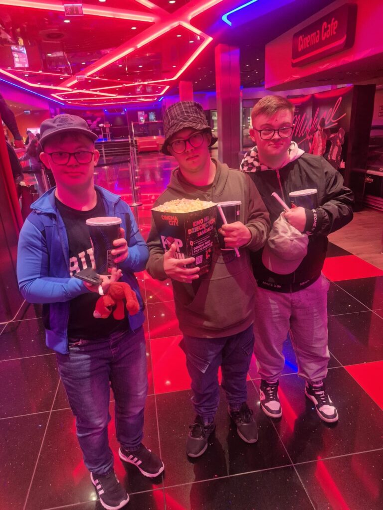 Trzech uczestników siedzących na kinowych fotelach z napojami i popcornem podczas wspólnego wyjścia do kina