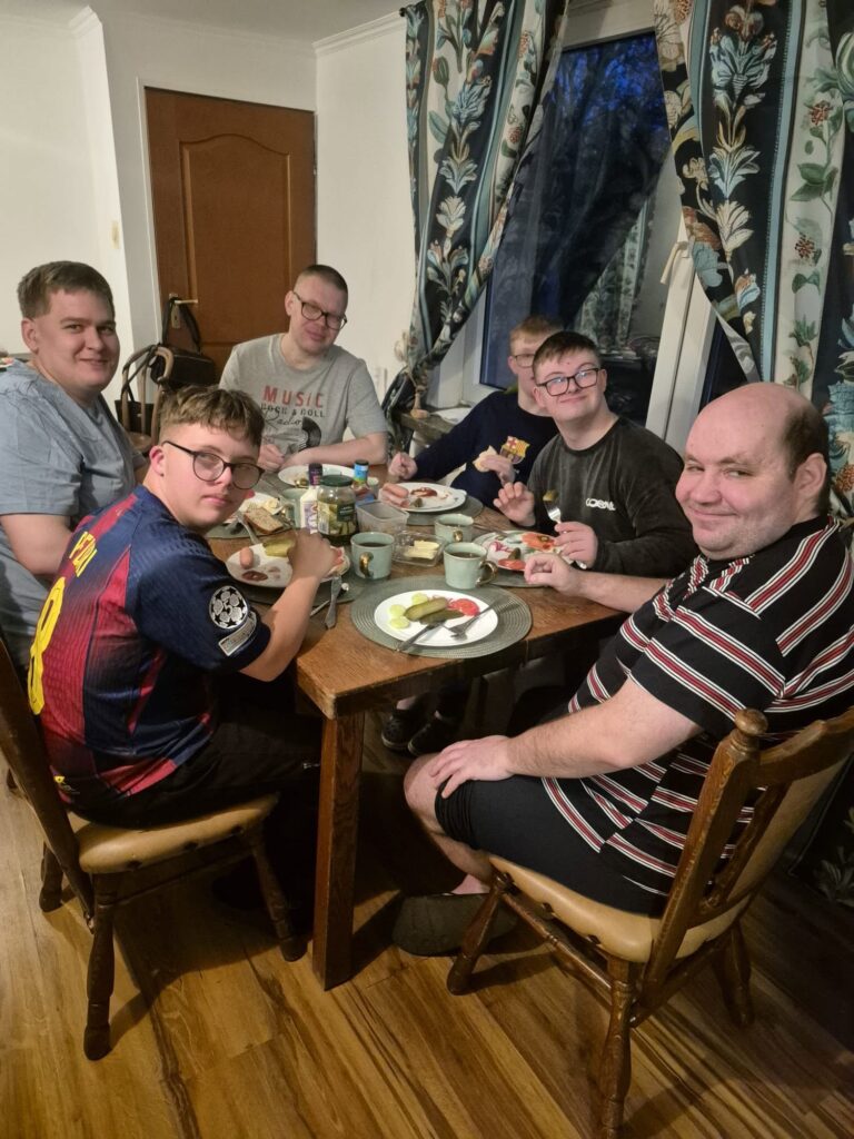 Grupa uczestników siedzących przy stole i jedzących wspólnie podczas pobytu w domu treningowym