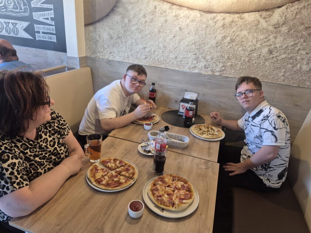 Uczestnicy pobytu w domu treningowym siedzący przy stole podczas wspólnego posiłku z pizzą