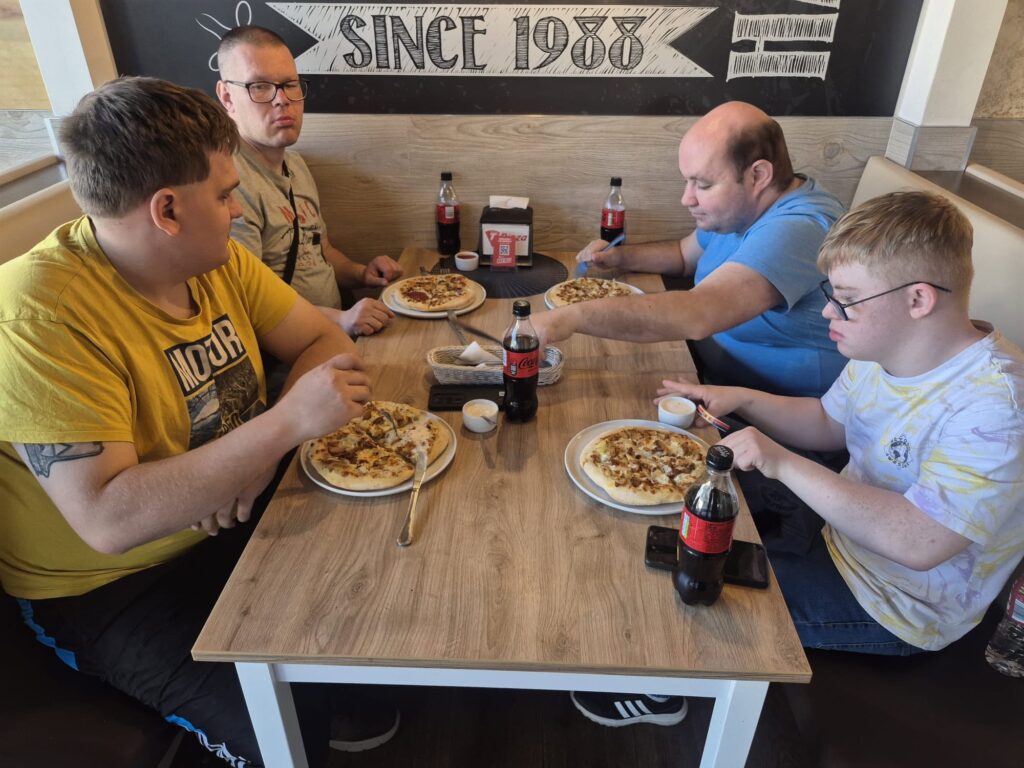 Uczestnicy pobytu w domu treningowym siedzący przy stole podczas wspólnego posiłku z pizzą