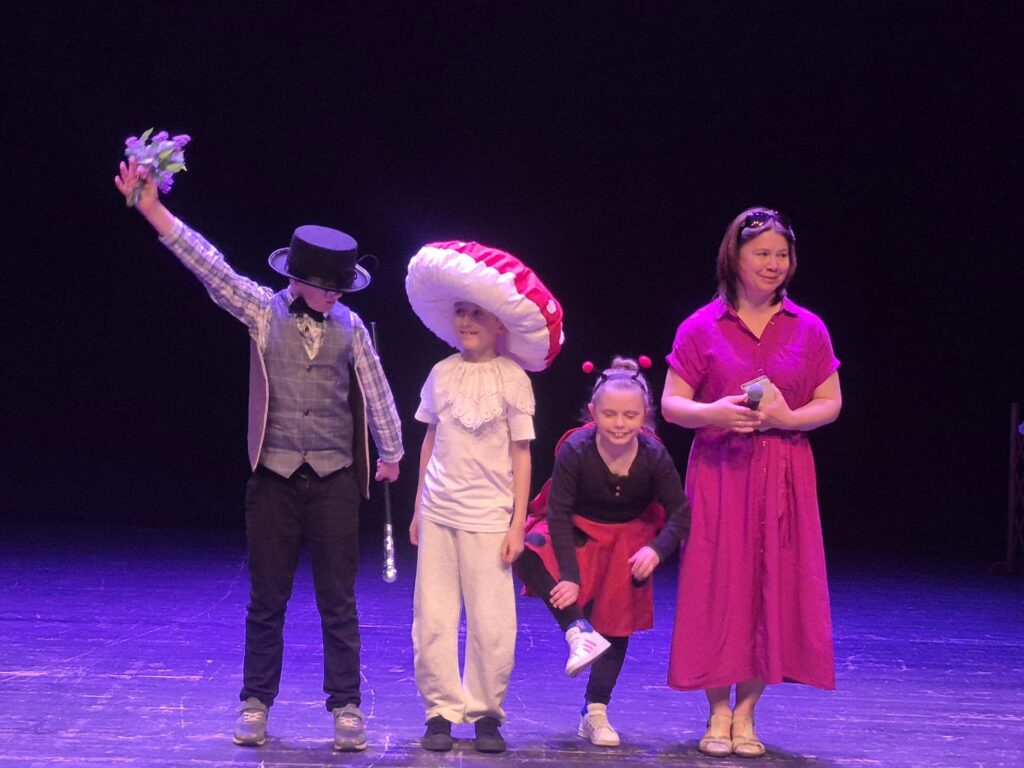 Uczestnicy przedstawienia stojący na scenie w teatralnych kostiumach podczas spektaklu