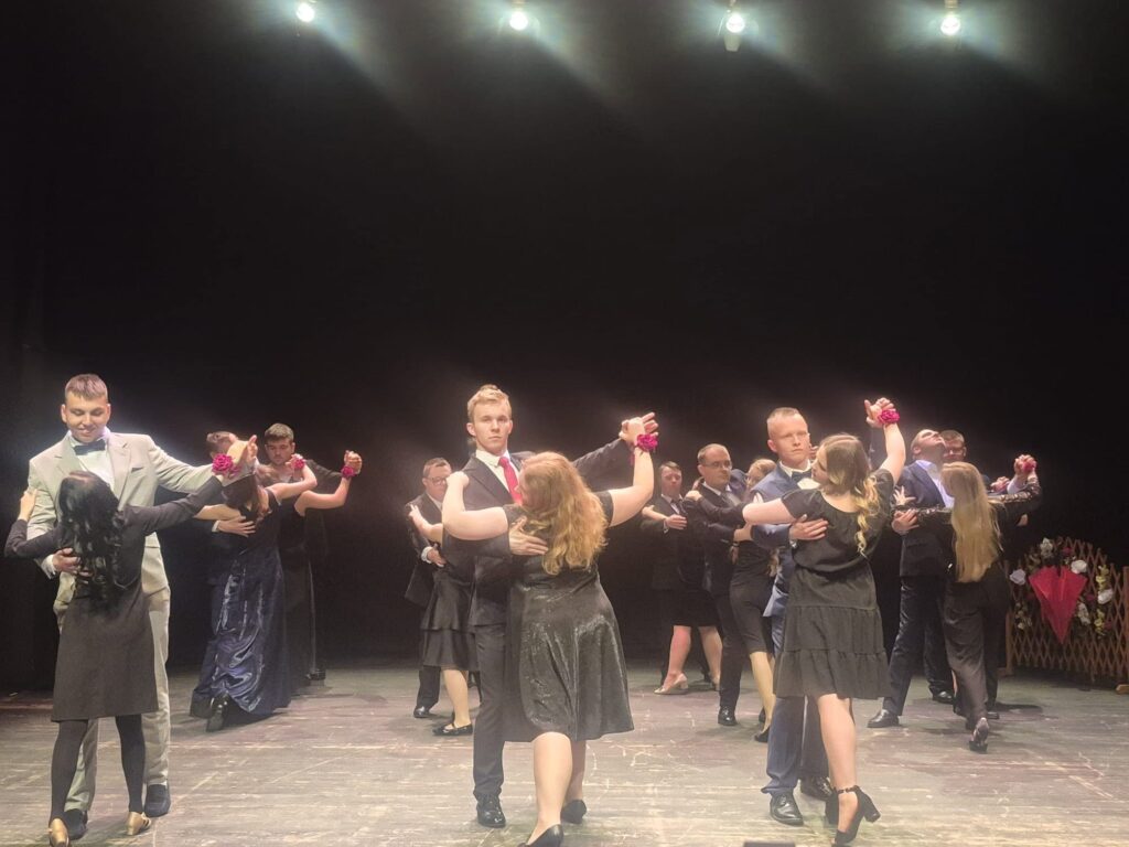 Uczestnicy wydarzenia tańczący w parach na scenie podczas artystycznego występu