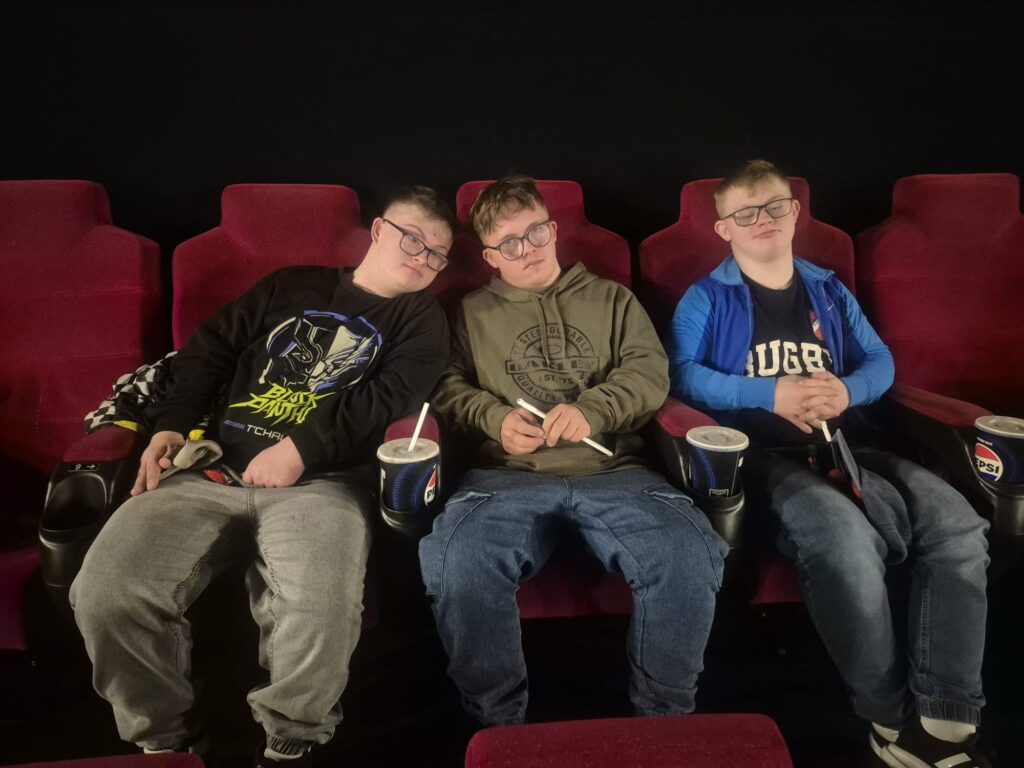 Trzech uczestników siedzących na kinowych fotelach z napojami i popcornem podczas wspólnego wyjścia do kina