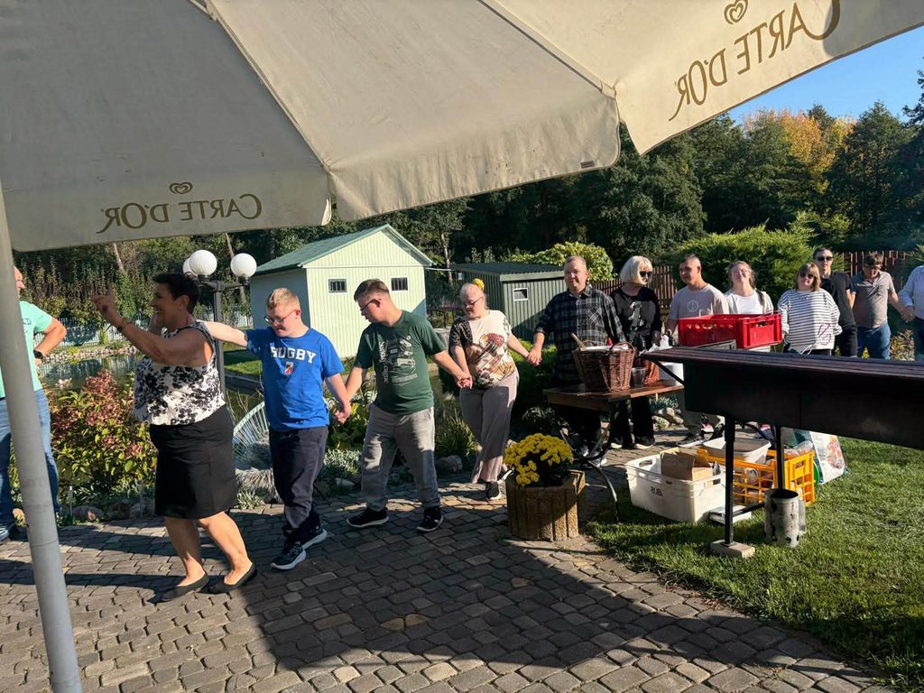 Uczestnicy pikniku integracyjnego biorą udział we wspólnej zabawie ruchowej na terenie ogrodu.