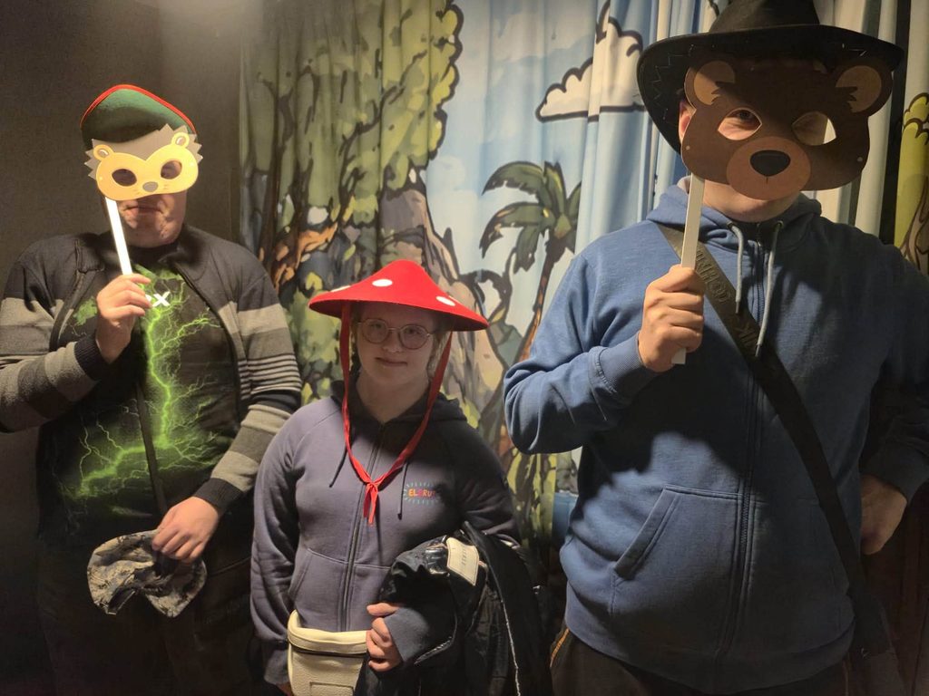 Uczestnicy wycieczki pozują do zdjęcia w tematycznej scenografii w Muzeum Dobranocek. Trzy osoby trzymają maski i mają na sobie bajkowe nakrycia głowy.