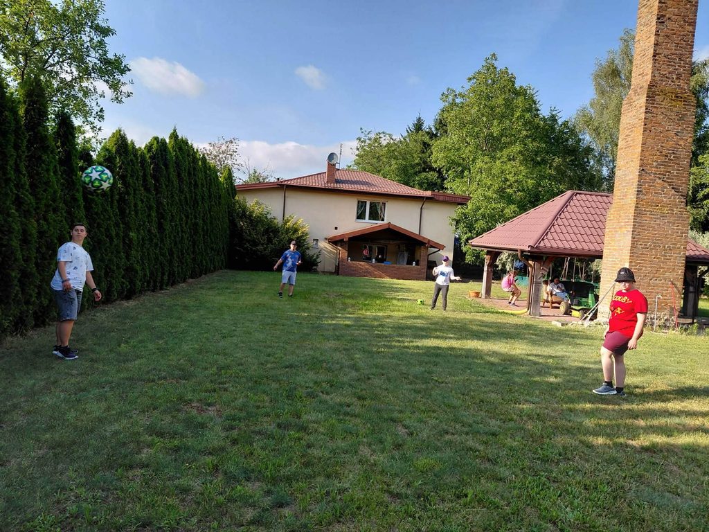Uczestnicy świetlicy biorą udział w rekreacyjnej grze z piłką na trawiastym terenie przy ośrodku.